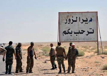 Syrian troops and pro-government gunmen standing next to a sign in Arabic which reads - 'Deir el-Zour welcomes you'