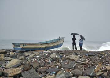 File pic - Two men hold umbrellas to protect themselves from the rain as they stand next to a fishing boat on the Arabian Sea coast in Thiruvananthapuram

