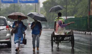 Commuters cross a road during a rainfall, in New Delhi, on Wednesday
