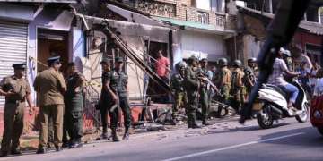 Sri Lanka's army soldiers and police personnel stand near a vandalized building in Digana, a suburb of Kandy.