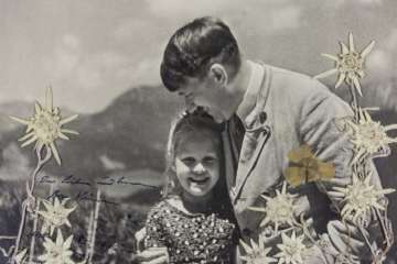 The black-and-white image taken by Heinrich Hoffmann and inscribed by Hitler in dark blue ink shows him smiling as he embraces Rosa Bernile Nienau in 1933 at his mountainside retreat. 