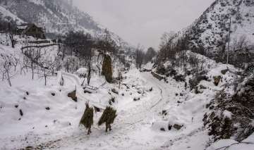 Villagers carry hay bales as they walk a snow-covered trail downhill