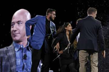 Security removes a protestor, second from left, from the stage as Amazon CEO Jeff Bezos speaks at the the Amazon re:MARS convention