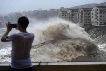  a man uses his mobile phone to record waves crashing on the shore as typhoon Lekima approaches the 