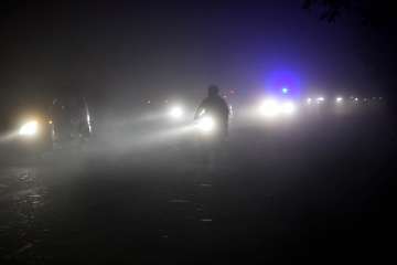 Vehicles ply at a road with headlights on during a cold and foggy night in New Delhi