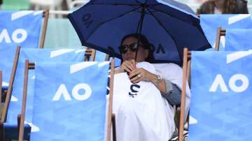 A spectator sits under an umbrella as rain stops play on the outside courts during the first round singles matches at the Australian Open tennis championship in Melbourne