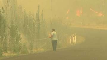 In this image made from video taken Dec. 21, 2019, a man sprays water on a fire in Lithgow, New South Wales state, Australia.