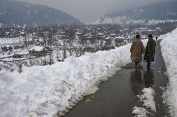 Srinagar: Men walk on a road along a snow-covered village after heavy snowfall at Ferozpora, Tangmarg in Baramulla district of north Kashmir