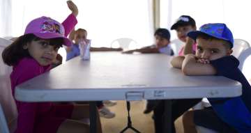 Kindergarten students from a school sit at a plastic table as they attend class.  AP Photo (File)