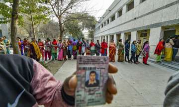 Voters stand in a queue to cast votes during the Delhi Assembly election at a polling station in Baprola village, New Delhi,