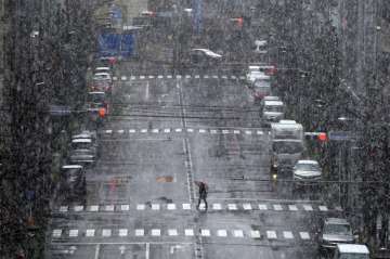A woman walks in falling snow in Tokyo Saturday, March 28, 2020. Tokyo Gov. Yuriko Koike has repeate