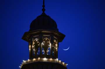An illuminated view of one of the minarets of Jama Masjid in the backdrop of a moon on the first day of holy month of Ramzan