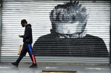 A shopper wears a mask as he passes by a closed storefront featuring a portrait of actor James Dean 