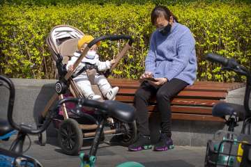 A woman and an infant wear face masks as they sit in the sun in Beijing, Wednesday, April 1, 2020. C