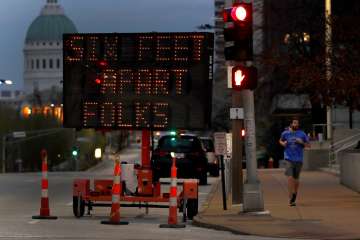 A person jogs past a sign encouraging social distancing Thursday, April 2, 2020, in St. Louis. The c