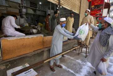 A shopkeeper deals customers with distance to help avoid the spread of coronavirus, in Peshawar, Pak