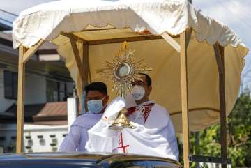 A Catholic priest wearing a protective mask holds a Monstrance with the Sacred Host as he rides a pi