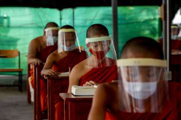 Novice Buddhist monks with protective masks and face shields, seated to maintain social distancing p