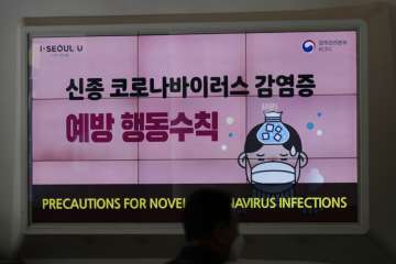 A man wearing a face mask passes by a screen displaying precautions against the coronavirus at the D