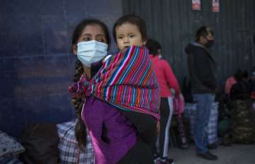 Judith Quispe, 24, carries her 9-month-old son Dilan, as they wait in line at a camp in Lima to regi