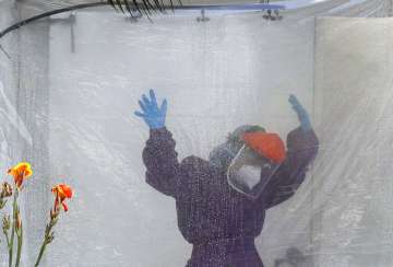 A health worker wearing a protective suit is disinfected inside a portable tent outisee the Gat Andr