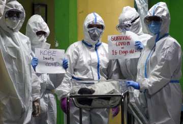 Health workers wearing protective suits holds signs beside a 16-day-old baby who recovered from COVI