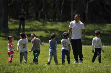 Children accompanied by a man play at a public park as kindergarten and primary schools still remain