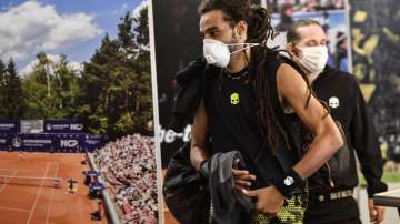 Germany's tennis player Dustin Brown wears a face mask as he walks by a poster at a pro-tennis tournament at a local base tennis academy in Hoehr-Grenzhausen, Western Germany, Friday, May 1