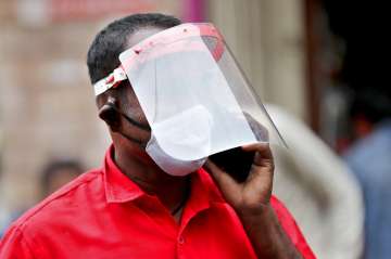 An Indian trader wears a face shield and mask as he talks on his mobile phone at a wholesale fruit m