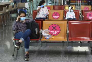 Passengers wearing face masks are seated maintaining social distancing before boarding their flight 