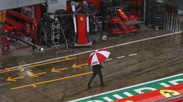 A man with an umbrella walks in the rain in the pit lane prior the delayed third practice session for the Styrian Formula One Grand Prix at the Red Bull Ring racetrack in Spielberg, Austria, Saturday, July 11