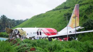 Officials stand on the debris of the Air India Express flight that skidded off a runway while landin