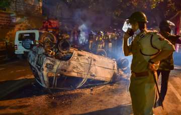 Bengaluru: Police stand next to the charred remains of a vehicle vandalised by a mob over a social media post by a relative of a MLA, in Bengaluru, Wednesday morning, Aug. 12, 2020.