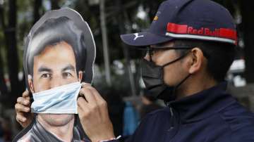 A man adjusts a face mask on a promotional cardboard cutout of Sergio "Checo" Perez, as a small group of fans gathers to celebrate his first Formula One win, at the Sakhir Grand Prix in Bahrain, near the Angel of Independence monument in Mexico City, Sunday, Dec. 6