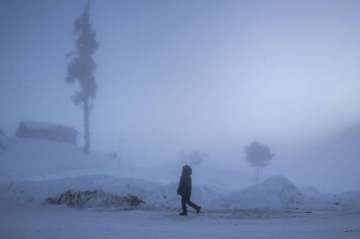An Indian tourist enjoys a morning walk on a snow-covered road on a cold and foggy morning in Gulmar