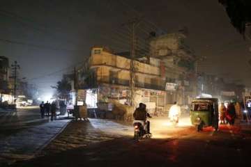 People are silhouetted on vehicles headlights on a dark street during widespread power outages in Ra