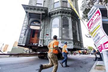 Workers pass a Victorian home as a truck pulls it through San Francisco on Sunday, Feb. 21, 2021. The house, built in 1882, was moved to a new location about six blocks away to make room for a condominium development