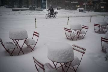 A man delivers food on his electric bicycle as he rides past snow-covered dining tables in midtown d