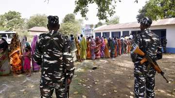 Paramilitary jawans guard as people wait in a queue to cast their votes at a polling station during the first phase of West Bengal Assembly elections, at Chandrapur in Lalgarh.