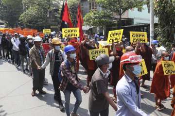 Monks and protesters hold placard and gesture with a three-finger symbol of resistance, as they prot