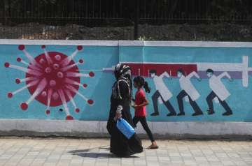 A woman along with a girl walk past a graffiti, depicting the coronavirus in Mumbai