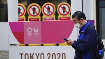 A man wearing a protective mask to help curb the spread of the coronavirus walks past a banner for the Tokyo 2020 Olympic and Paralympic Games in Tokyo Tuesday, May 11
