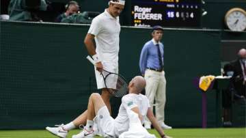 Switzerland's Roger Federer talks to Adrian Mannarino of France as he lies on the ground in pain during the men's singles first round match against on day two of the Wimbledon Tennis Championships in London, Tuesday June 29