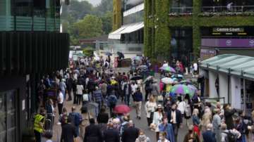 Crowds walk around the grounds during a rain delay on day one of the Wimbledon Tennis Championships in London, Monday June 28