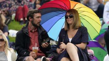 People shelter under an umbrella during a rain delay on day one of the Wimbledon Tennis Championships in London, Monday June 28