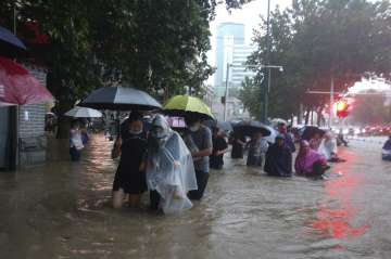 People move through flood water after a heavy downpour in Zhengzhou city, central China's Henan province on Tuesday, July 20, 2021. Heavy flooding has hit central China following unusually heavy rains, with the subway system in the city of Zhengzhou inundated with rushing water and thousands of residents having to be relocated.