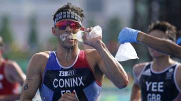 Dorian Coninx of France takes water as a volunteer holds out a bag of ice, during the run portion of the men's individual triathlon at the 2020 Summer Olympics, Monday, July 26