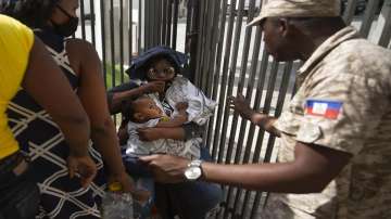 A Haitian police asks a woman to move away from a gate at the U.S. Embassy in Port-au-Prince, Haiti.