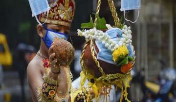 A child wearing a face mask and dressed?as Lord Krishna breaks an earthen pot on the occasion of Janmashtami?