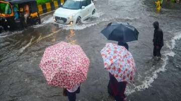 Commuters wait to cross a waterlogged street as vehicles ply during heavy rainfall in Maharashtra.